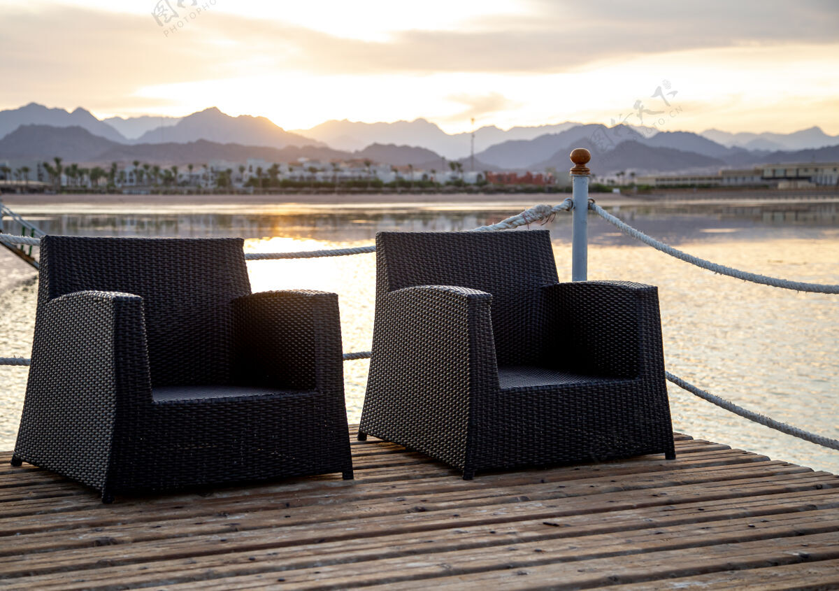 地中海两张空椅子放在木墩上 在夕阳下俯瞰群山剪影风景码头