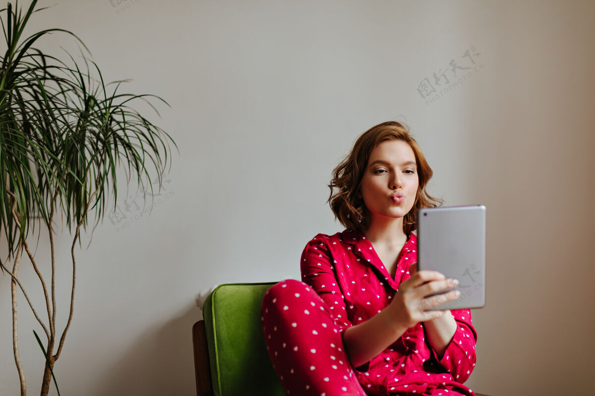 设备可爱的女人用亲吻的表用数码平板电脑拍摄穿着睡衣的卷发女人的室内照片花卉睡衣休闲