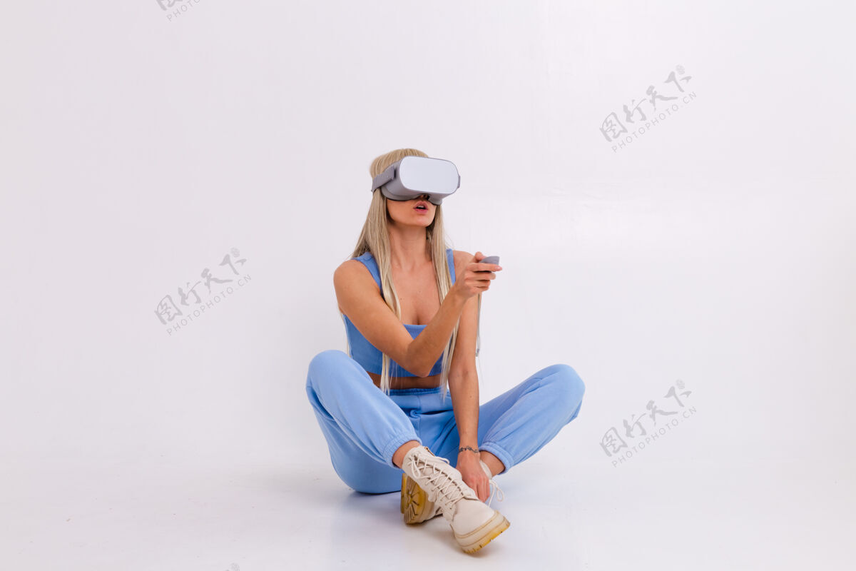 观看摄影棚照片中一个年轻迷人的女人穿着温暖的蓝色时尚西装戴着虚拟现实眼镜现实女性体验