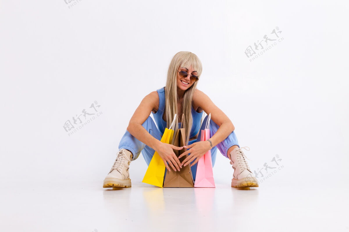 包装年轻金发女郎的时尚写真 长着华丽的直发 带着五颜六色的购物袋 在摄影棚里一头白色的头发上兴奋购物者姿势