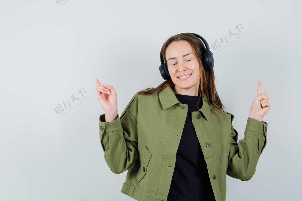 时尚穿着绿色夹克 戴着耳机听音乐 看上去很有趣的年轻女子 正面视图青春时尚聆听