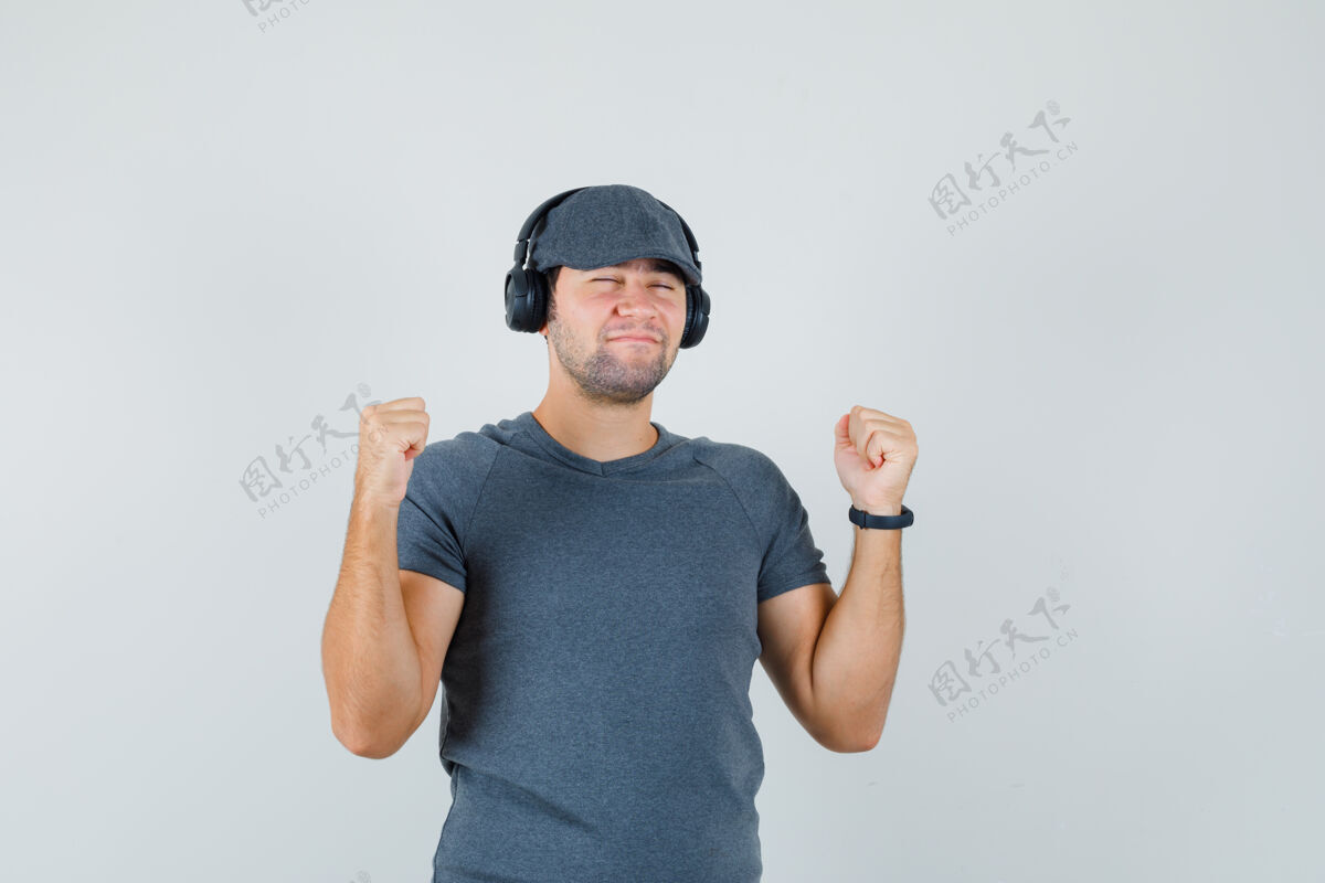 享受年轻的男性穿着t恤 戴着帽子 戴着耳机欣赏着音乐 看上去很高兴 前视图男孩微笑男人