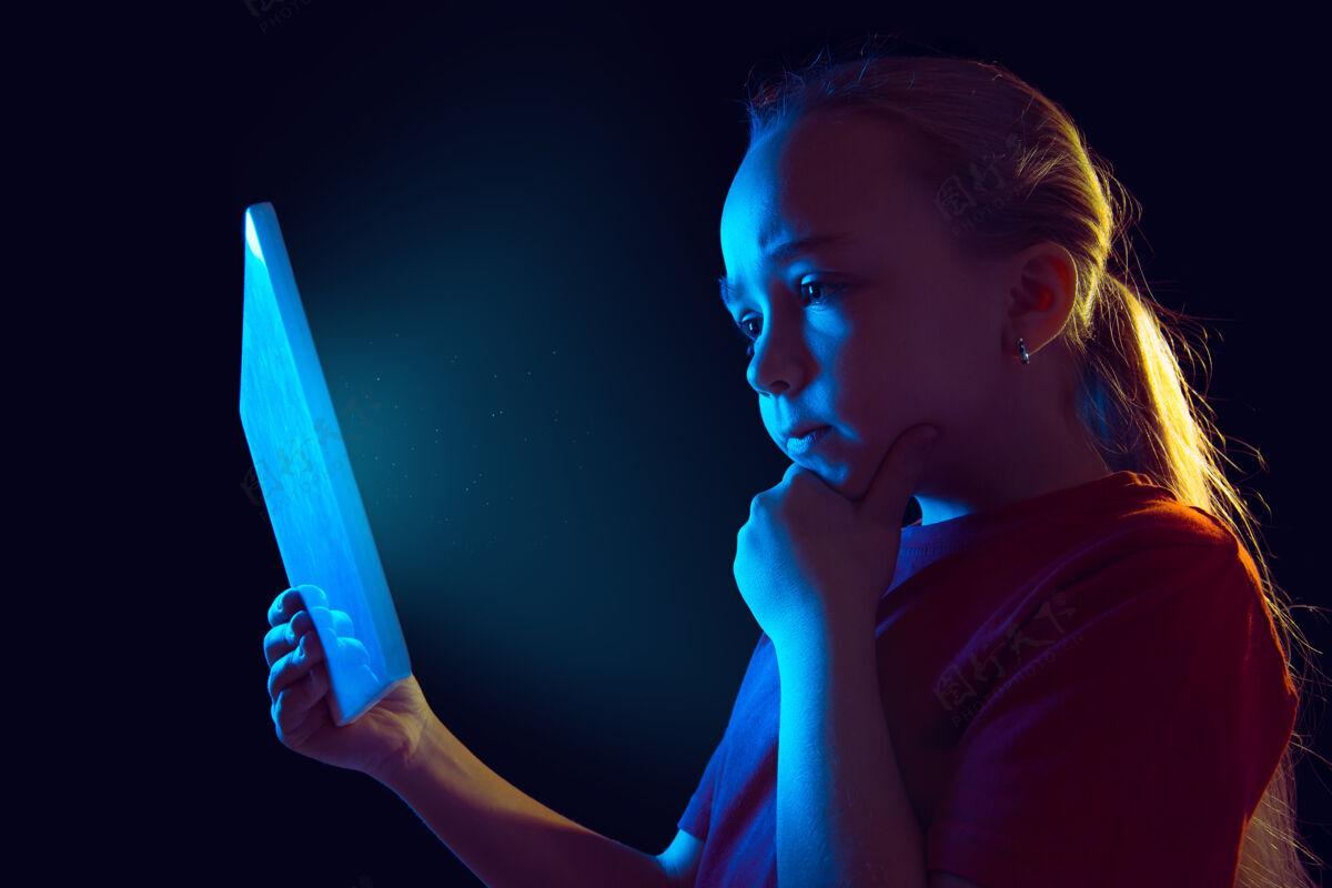 平板电脑体贴在霓虹灯下的黑暗工作室背景上的白种女孩肖像使用平板电脑的漂亮女模特梯度使用屏幕