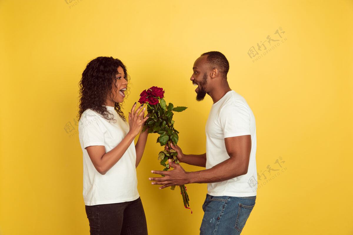 浪漫鲜花为微笑情人节庆祝 快乐的非洲裔美国夫妇隔离在黄色工作室背景黑色爱情表情