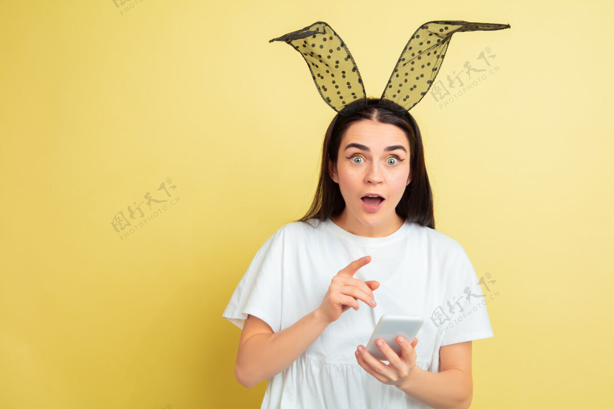 姜黄色震惊使用电话白人妇女作为复活节兔子黄色工作室背景复活节快乐的问候时尚有趣情感