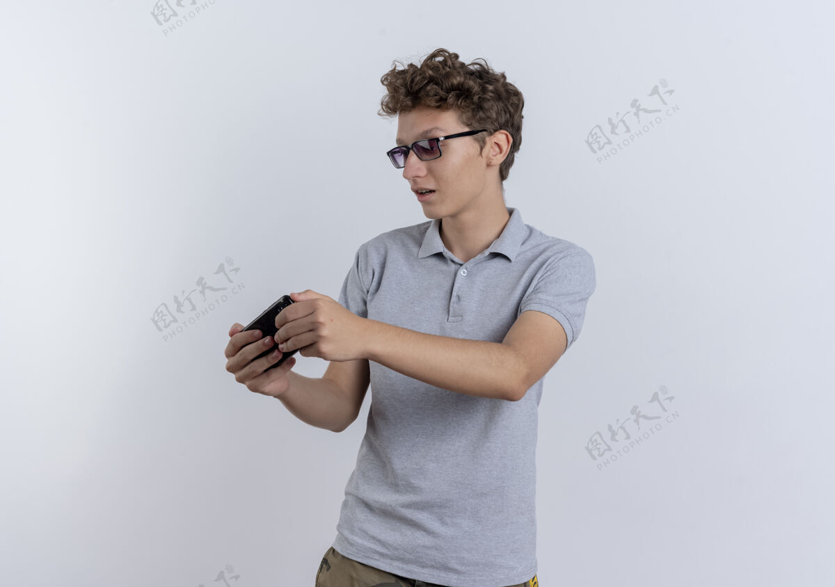 玩穿着灰色马球衫的年轻人站在白墙上看智能手机屏幕玩游戏游戏马球男人