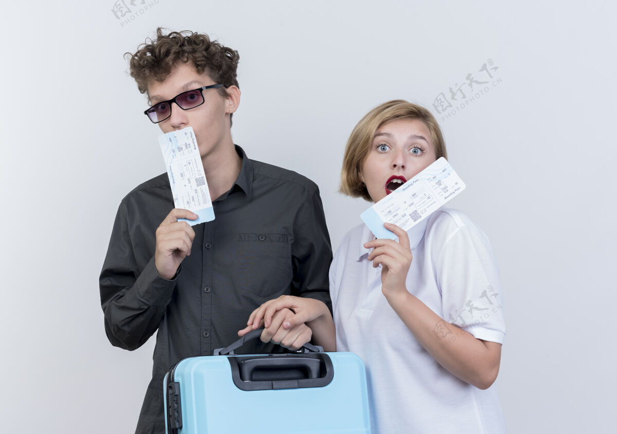站着一对年轻的游客 一男一女拿着机票和手提箱 站在白色的墙壁上 看上去既惊讶又惊讶男人惊奇飞机