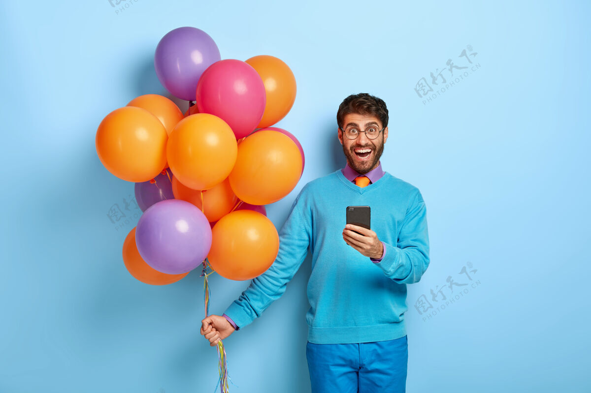 微笑满意的家伙拿着气球在蓝色毛衣里摆姿势庆祝毛衣男人
