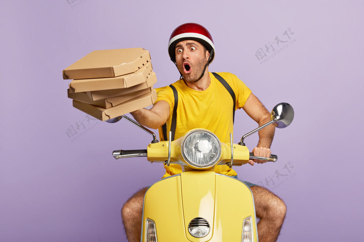 姿势超载繁忙送货员驾驶黄色滑板车 而持有比萨饼盒男人快速忙碌