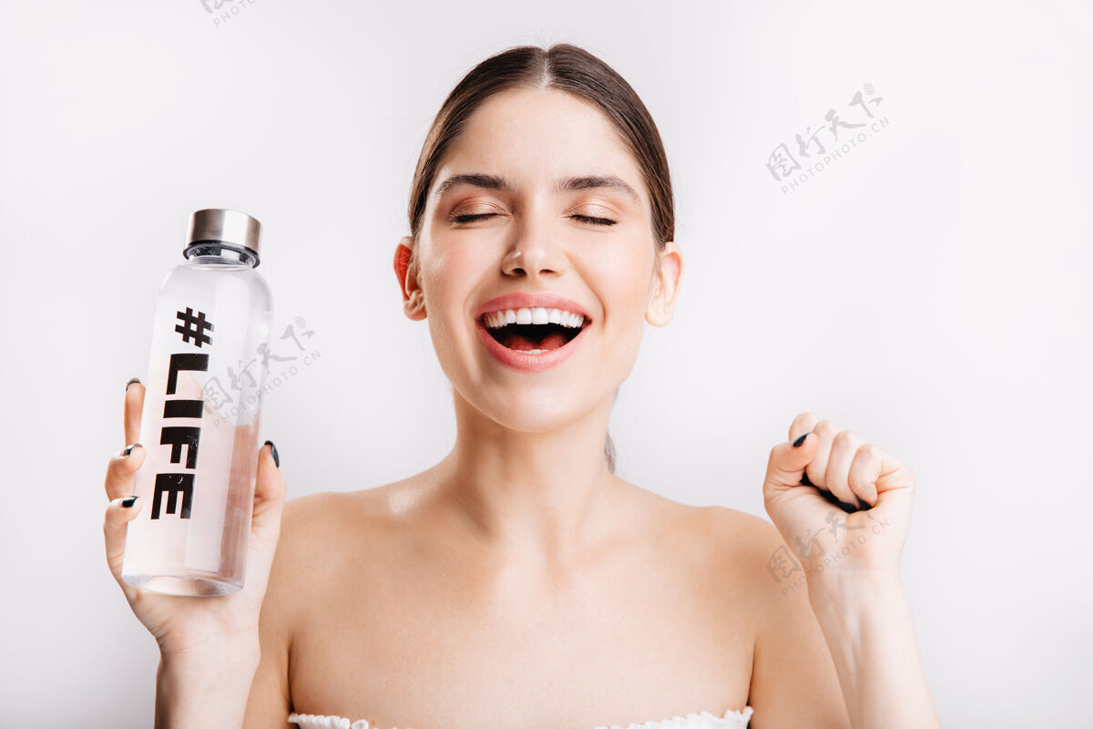 青春没有化妆的快乐女士的肖像 在隔离墙上拿着一瓶水愉快地摆姿势模特清晰斯帕