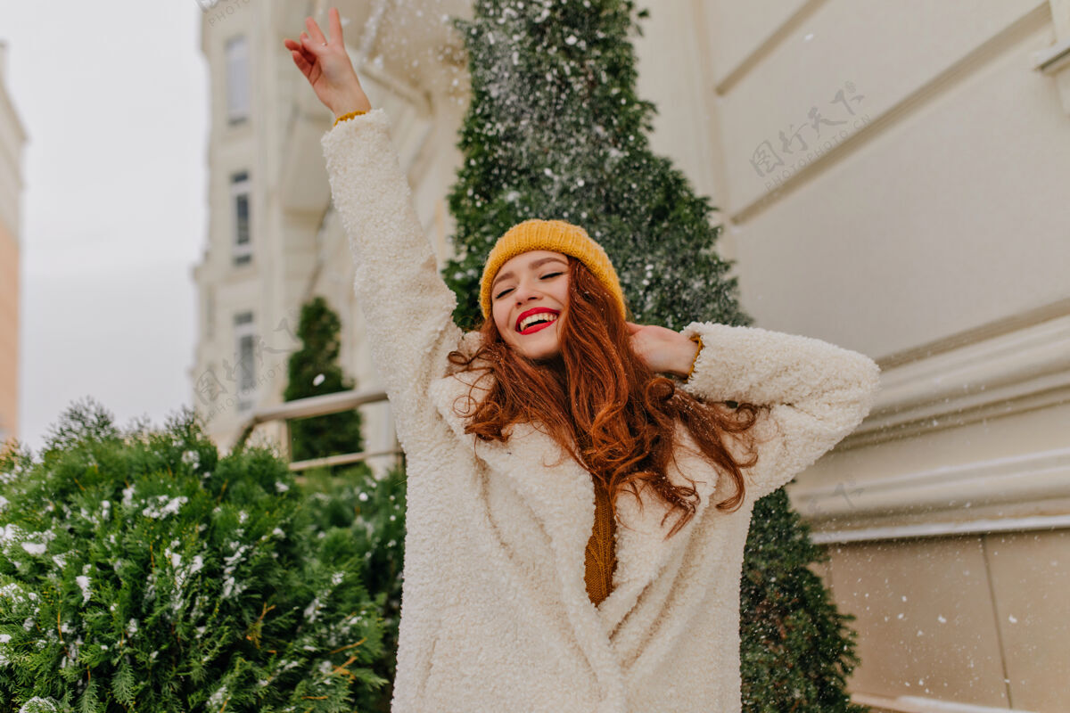 杉木时髦的红发女孩在雪下摆姿势笑着的白人妇女享受冬季周末的户外照片户外肖像女性