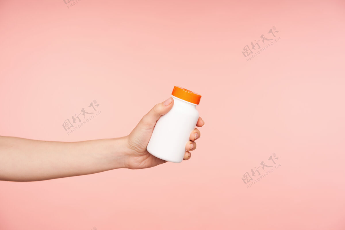白皙摄影棚照片的年轻女性的手与裸体美甲保持瓶与药片 而被隔离在粉红色的背景保健和美容的概念手臂护理复制空间