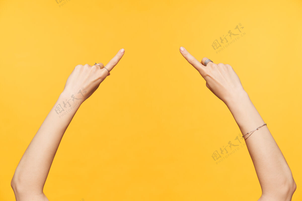成人你的手与裸体指甲保持食指抬高 同时显示在中间点 隔离黄色背景的女性手的水平镜头手势戒指手臂