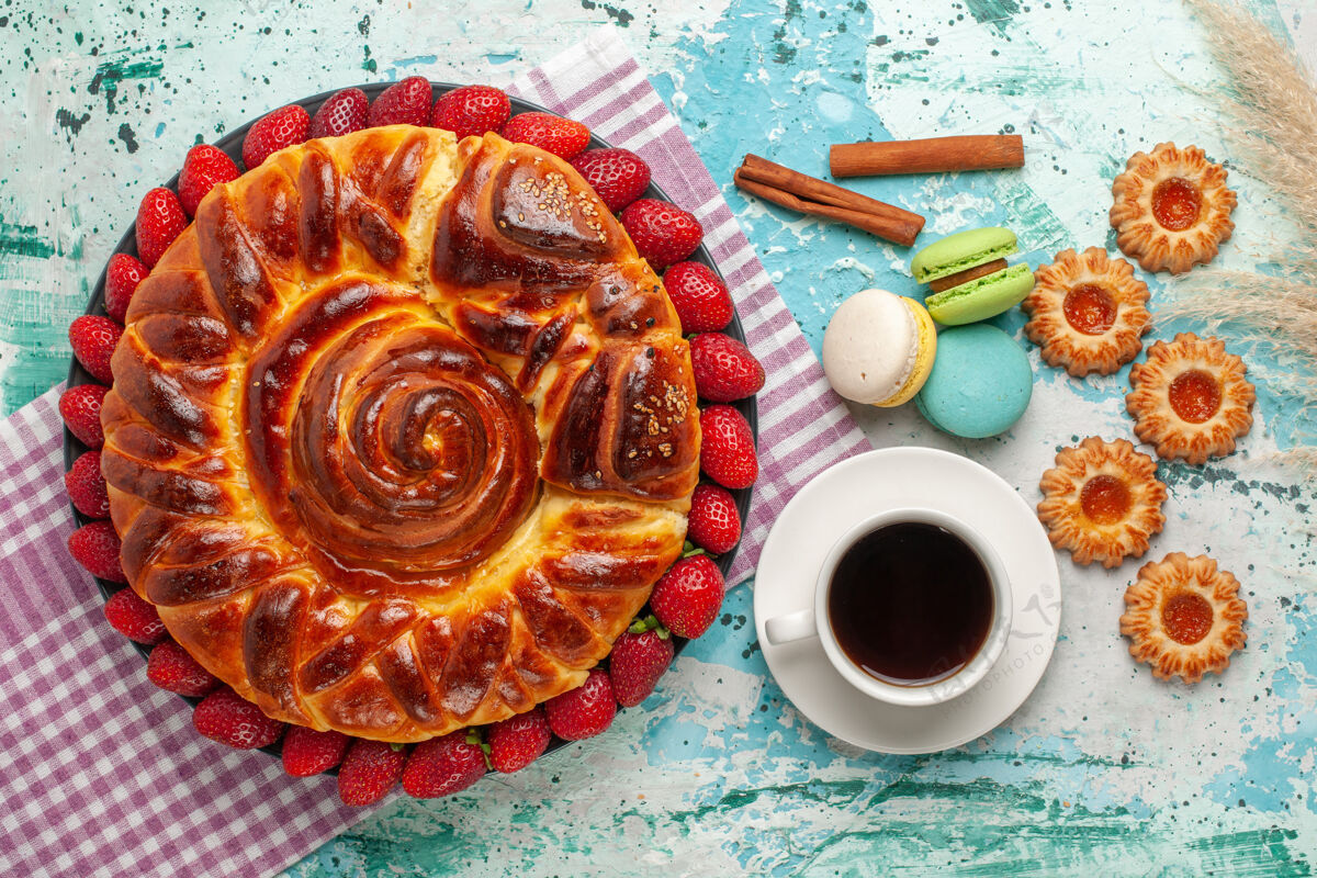 蛋糕俯瞰美味的派与新鲜的红色草莓麦卡龙和一杯茶在蓝色的表面饼干早餐糖果
