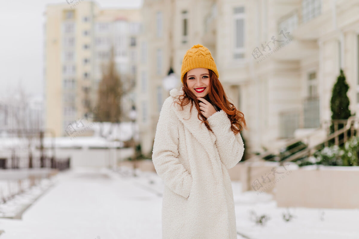 灵感美丽的白种人女孩在冬天的城市里散步穿着白大褂的姜黄色女人在街上摆姿势休闲寒冷寒冷的天气