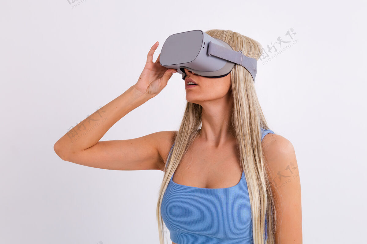 Vr摄影棚照片中一个年轻迷人的女子穿着温暖的蓝色时尚西装 戴着虚拟现实眼镜在白色的护目镜享受快乐
