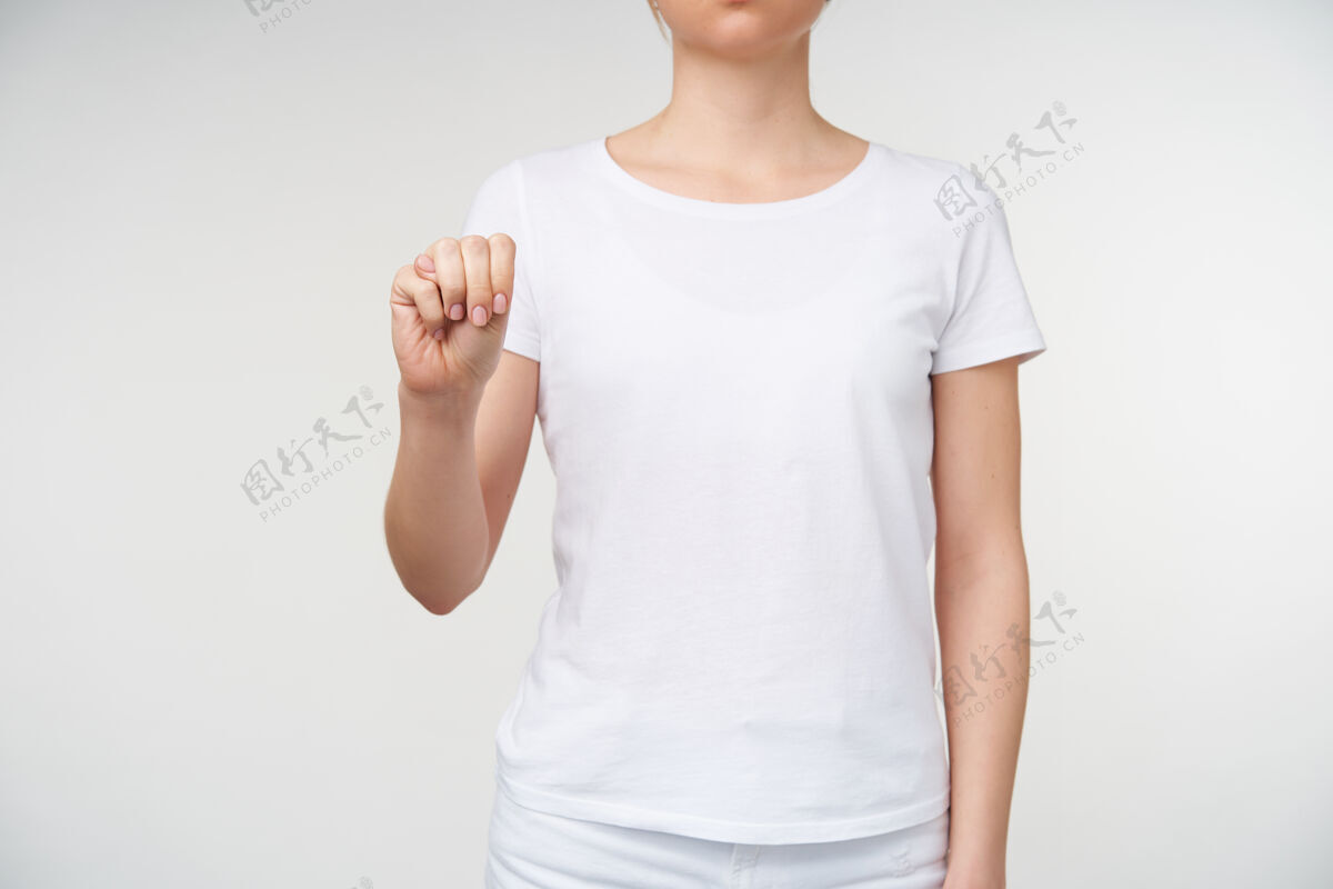 休闲摄影棚拍摄的一张照片 身着白色t恤的年轻女性紧握着她举起的手 同时在手语上形成字母m 隔离在白色背景上室内手臂成人