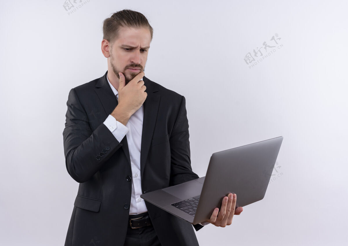 穿着穿着西装的帅哥拿着笔记本电脑站在白色的背景下沉思地看着它沉思站着思考