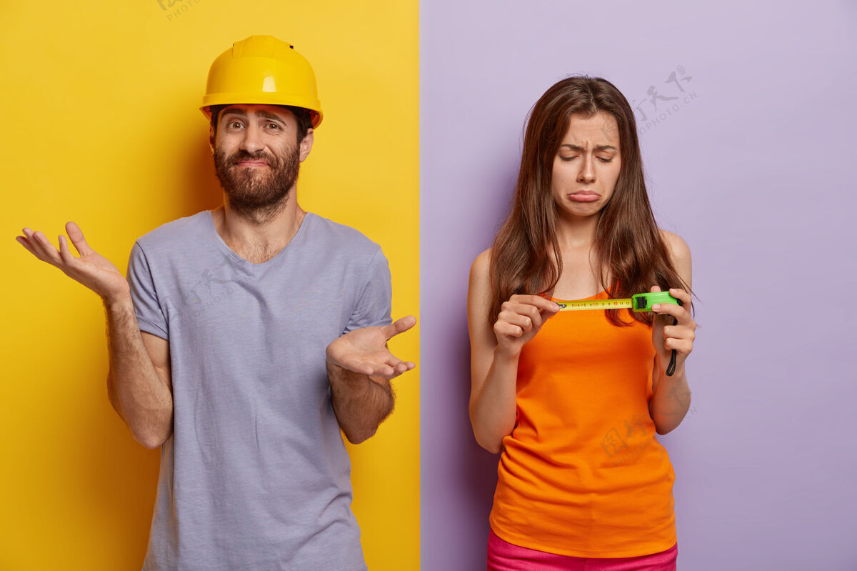 紫色家装概念不满悲伤的女人看卷尺 帮丈夫装修房子 犹豫不决的男人不知所措 摊开手掌 戴黄色安全帽 穿紫色t恤修理改善黄色