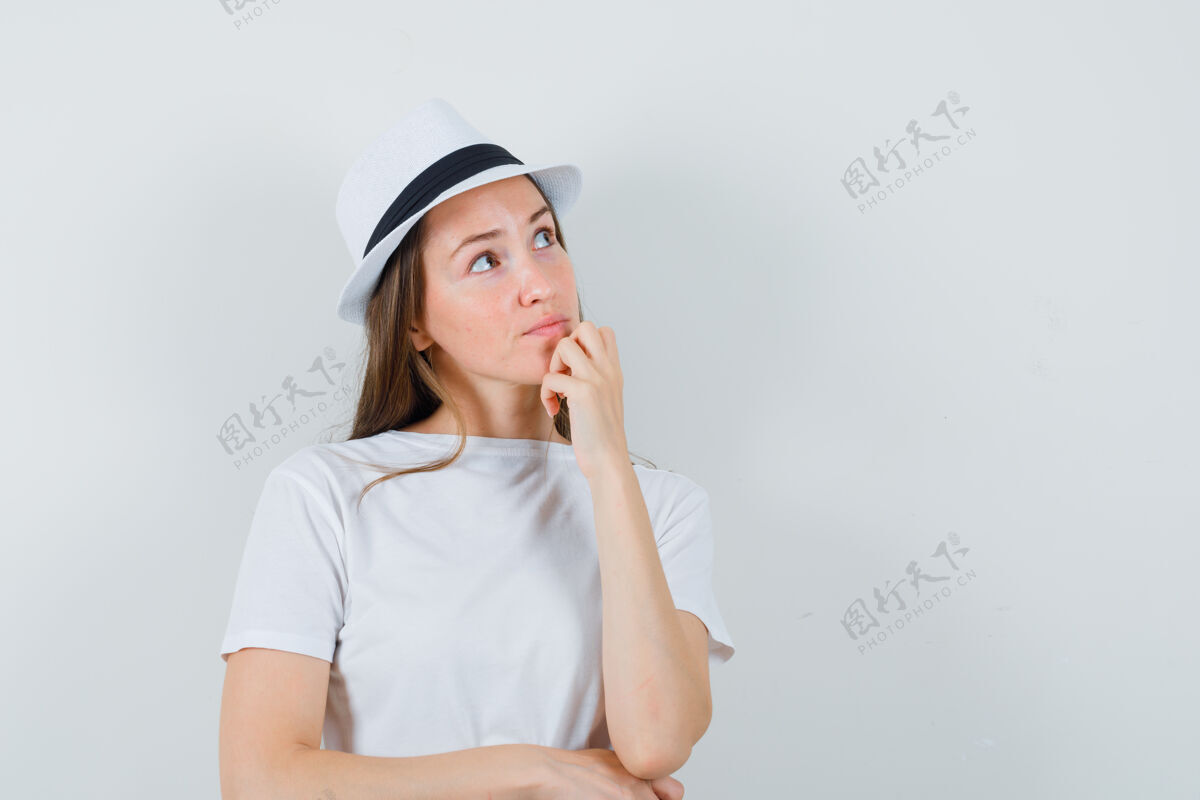 成人年轻女子手拉着下巴 穿着白色t恤 戴着帽子 看上去很体贴可爱积极乐趣