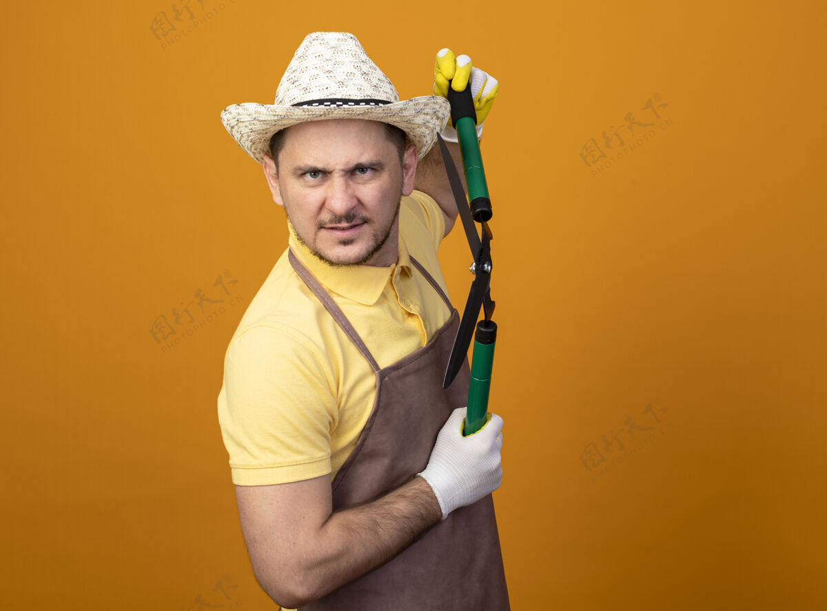 剪子一个年轻的园丁 穿着连体衣 戴着帽子 拿着树篱剪 满脸怒容愤怒帽子橙色