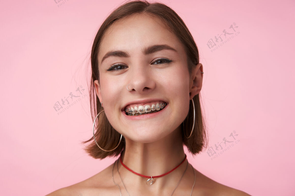 黑发摄影棚拍摄的年轻漂亮的快乐短发黑发女子与鲍勃发型是在很好的心情和微笑愉快的前面 隔离在粉红色的墙壁肖像戒指高兴