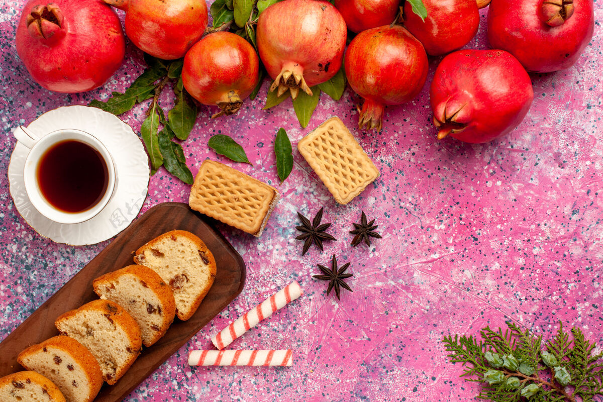 农产品在粉红色的桌子上 可以俯瞰新鲜的红石榴 切片蛋糕华夫饼和一杯茶蔬菜果汁萝卜