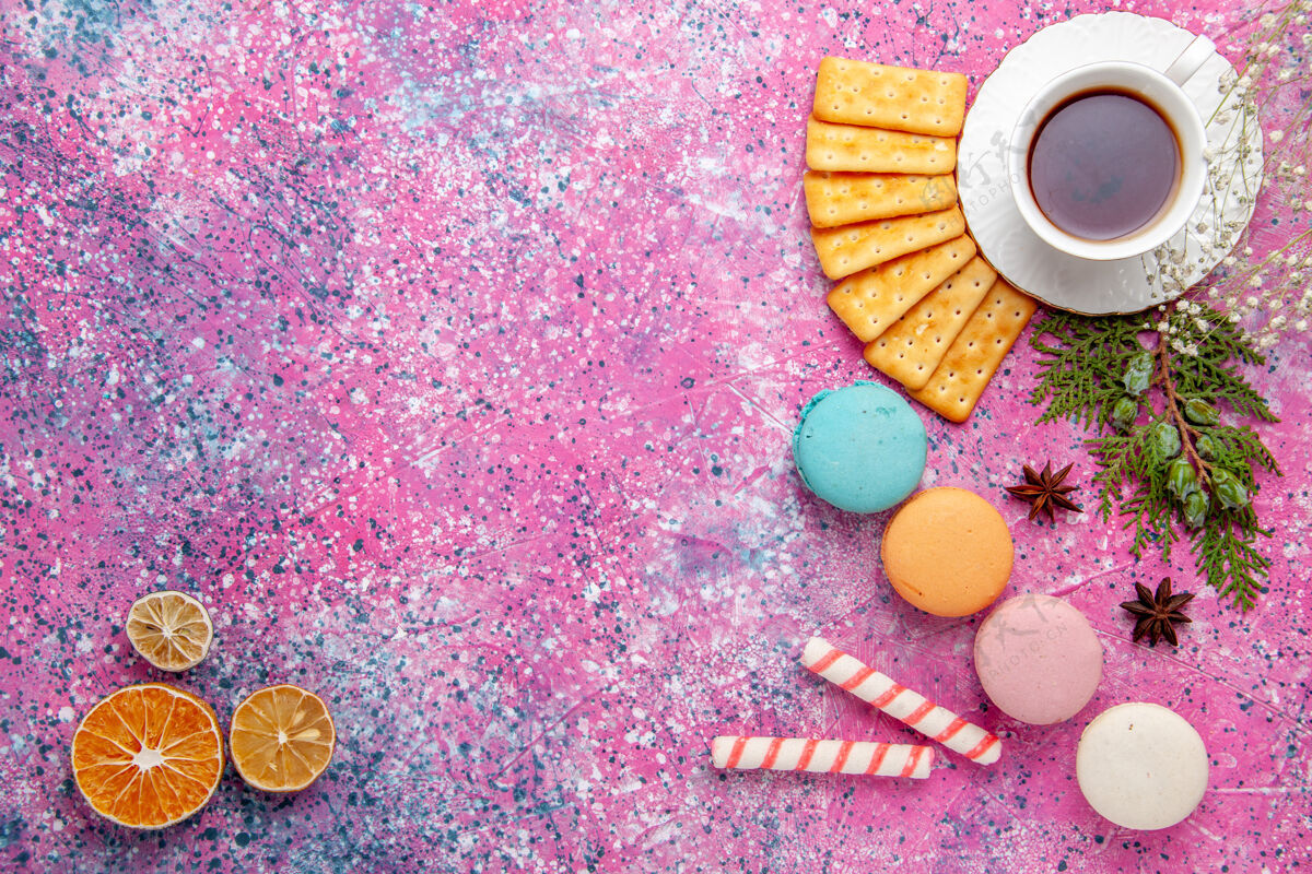 鲜花顶视一杯茶与饼干和法国马卡龙在粉红色的表面顶部麦卡龙饮料
