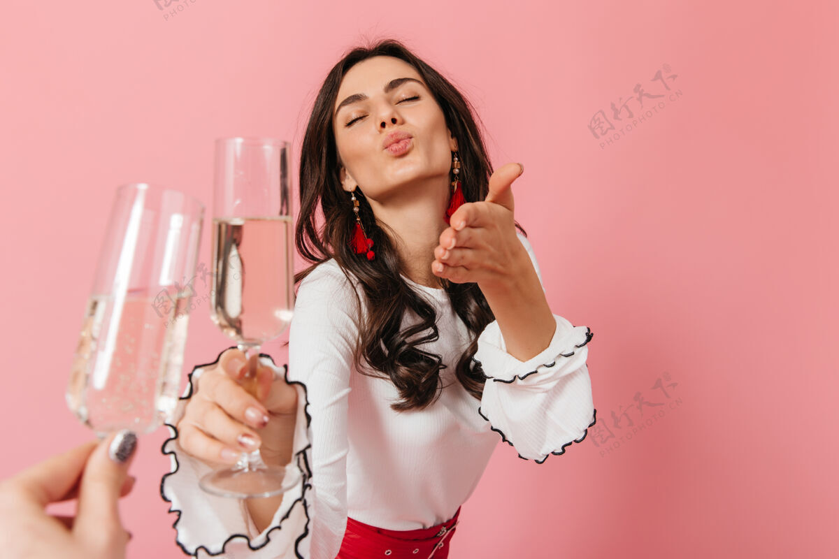 衣服戴着红耳环 穿着白衬衫的女士在孤立的背景下送上空气之吻和一杯起泡酒自信点女孩