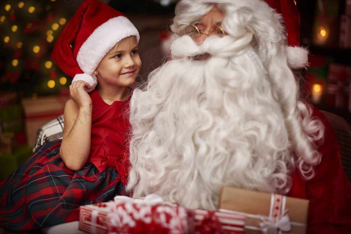 忙碌可爱的女孩坐在圣诞老人的膝盖上装饰品老年人奖励