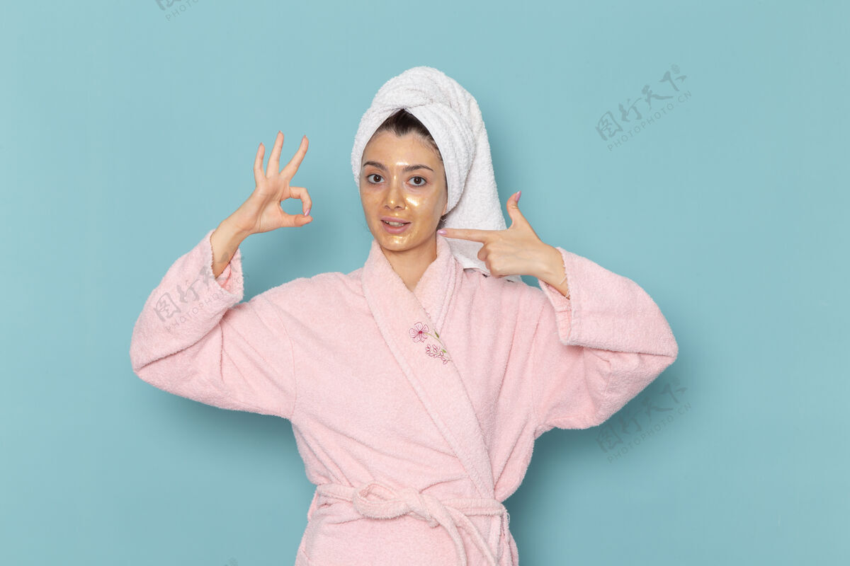 肖像正面图年轻女性穿着粉色浴袍淋浴后在蓝色墙面上摆姿势清洁美容净水自护霜淋浴后面清洁前面