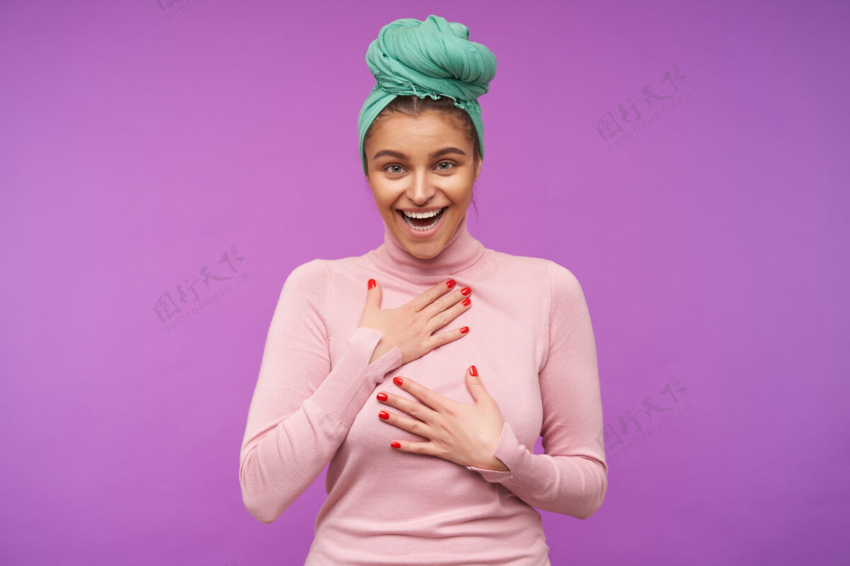 发髻快乐的年轻迷人的黑发女子穿着粉红色的马球衫 双手举在胸前 站在紫色的墙上开心地笑着休闲披肩衣服