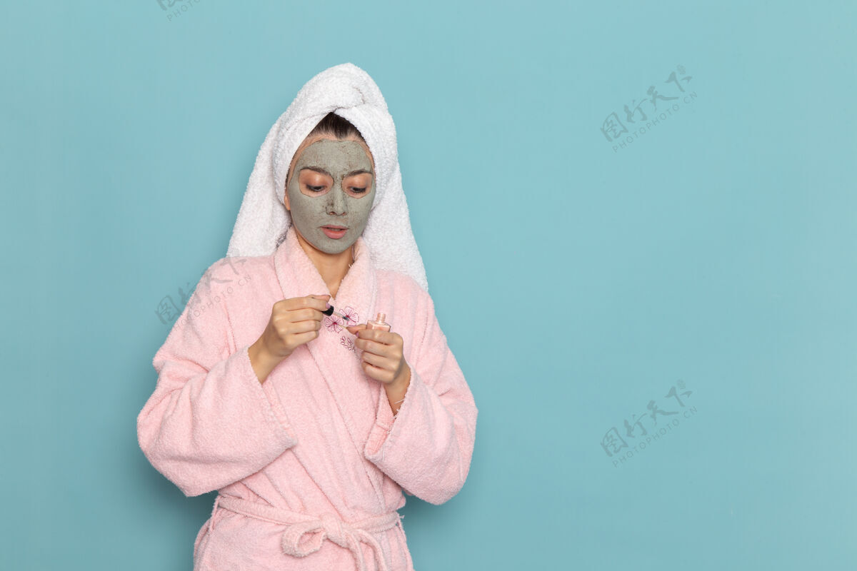 男人正面图身着粉色浴袍的年轻女性在淋浴后拿着指甲油在蓝色桌子上美容水霜自理淋浴抱着人淋浴