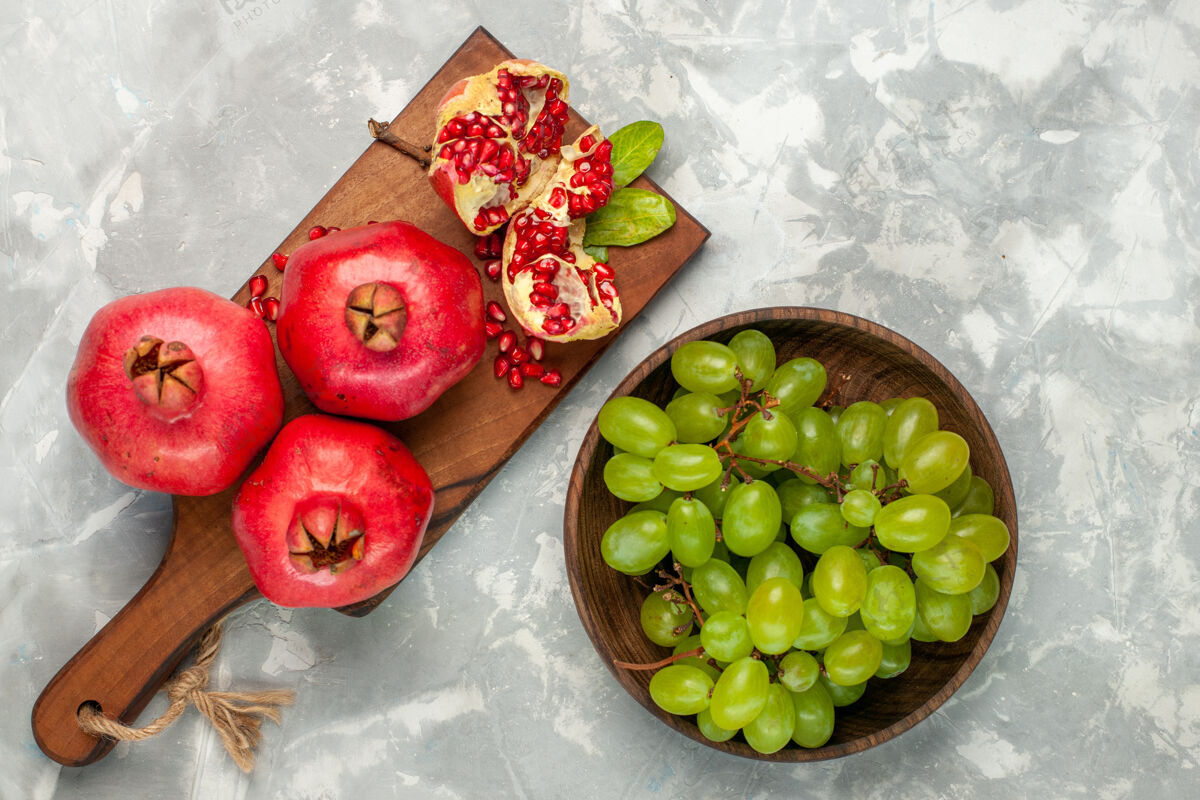 桌子顶视图新鲜的红色石榴酸和醇厚的水果与绿色葡萄在淡白色的办公桌上健康营养食物
