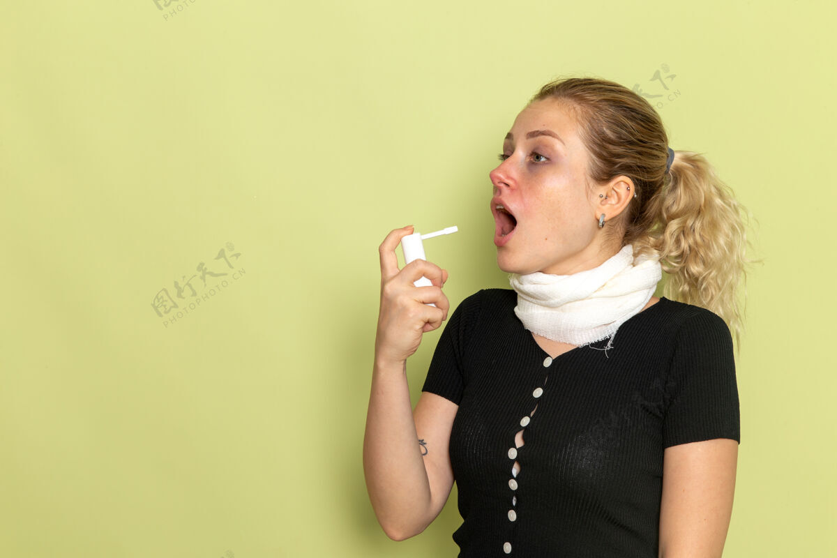 前面正面图年轻女性用白毛巾围住喉咙感觉很不舒服 用喷雾剂喷在绿墙上生病生病女性健康成人周围毛巾