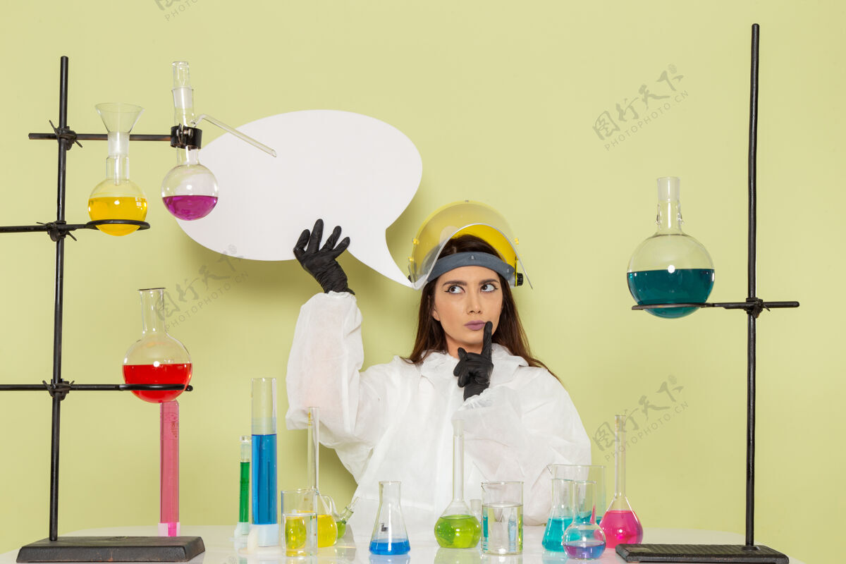 套装正面图身着特殊防护服的年轻女化学家手持浅绿色墙上的白色标牌化学工作女科学实验室正面外套年轻人