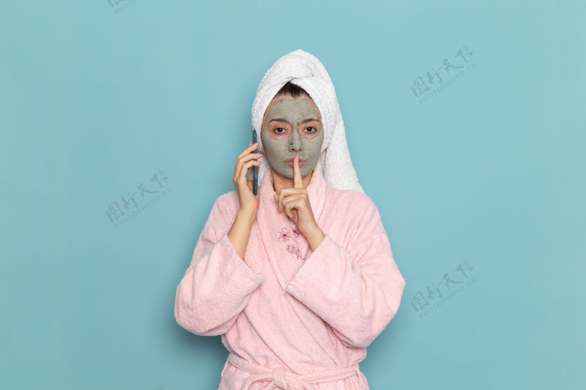 视图正面图身着粉色浴袍的年轻女性淋浴后在蓝色墙壁上讲电话美容净水自护霜淋浴年轻清洁淋浴