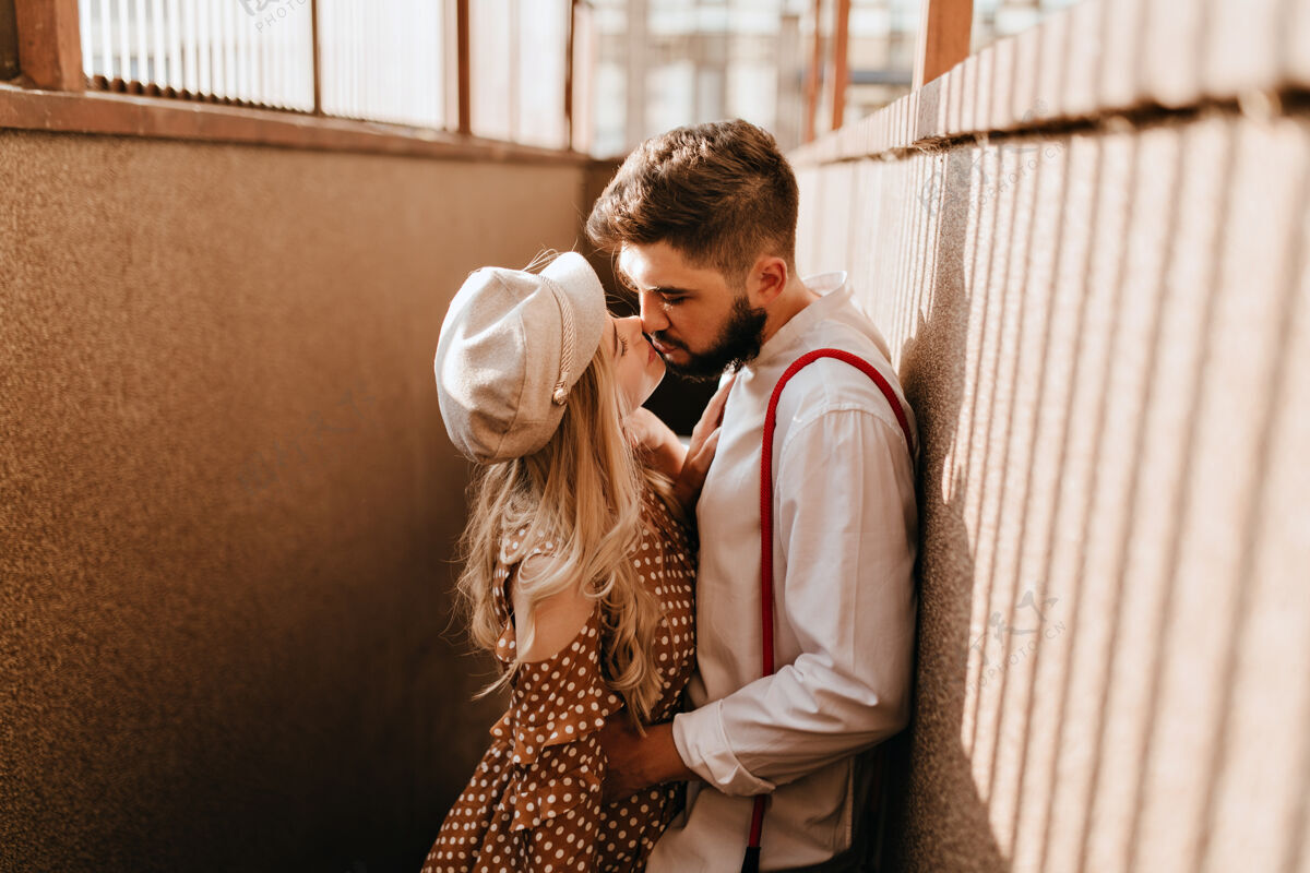 户外男人抱着他戴着米色帽子的金发女朋友一对浪漫的情侣享受阳光和接吻家庭红领夫妻