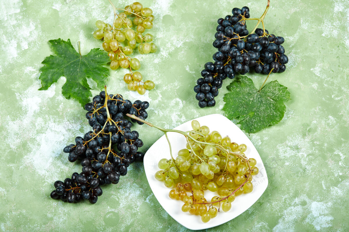 新鲜一盘白葡萄和黑葡萄的顶视图 绿色表面有叶子一串成熟潮湿
