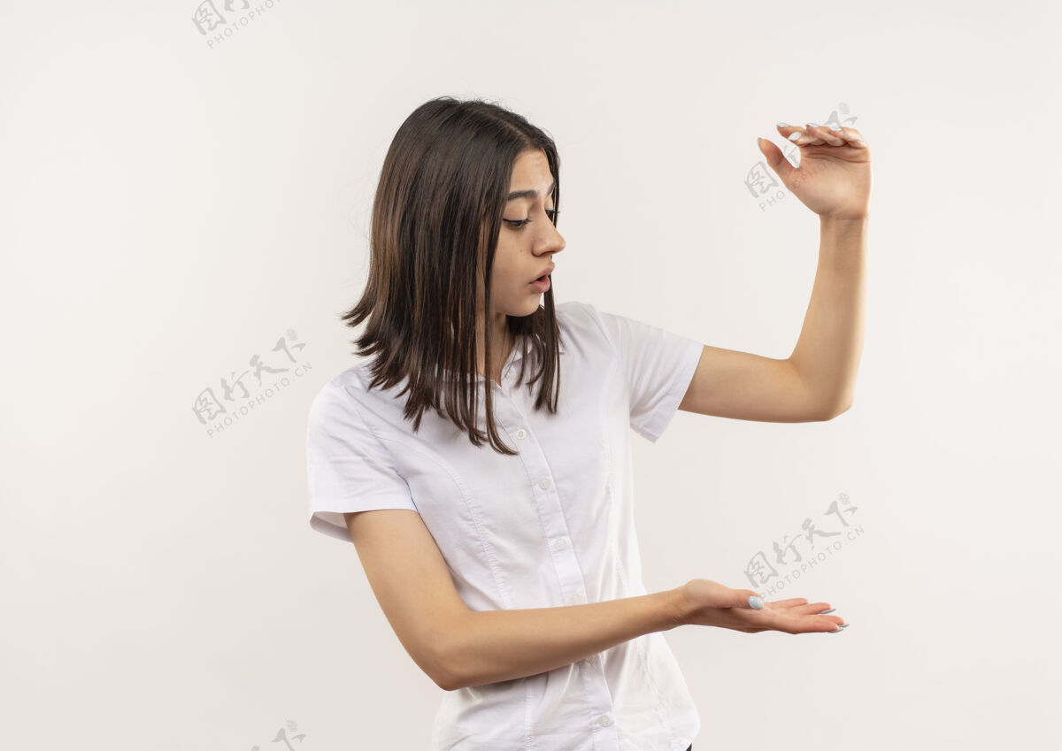 女人穿白衬衫的年轻女孩一边看一边用手做着展示身材的手势 一边站在白墙上测量标志测量站公民