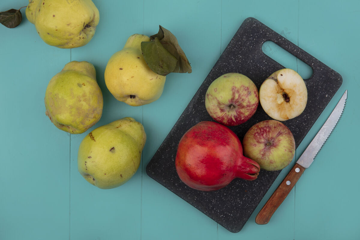 刀新鲜石榴和苹果的俯视图在一个黑色的菜板上 刀子上的木瓜被隔离在一个蓝色的背景上水果苹果顶部