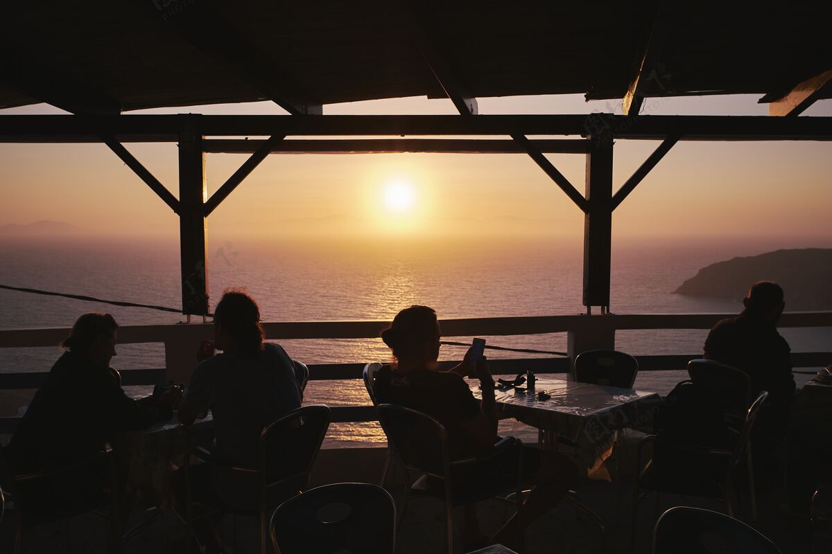 海滩在波塔莫斯海滩的咖啡馆里享受日落时光的人们的剪影 希腊倒影情侣岛屿