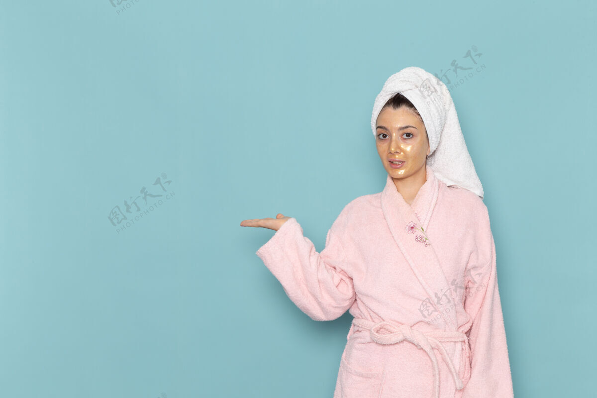 浴缸正面图身着粉色浴袍的年轻女性在蓝色墙壁上沐浴后 美丽的水浴霜自我护理淋浴女性浴袍成人