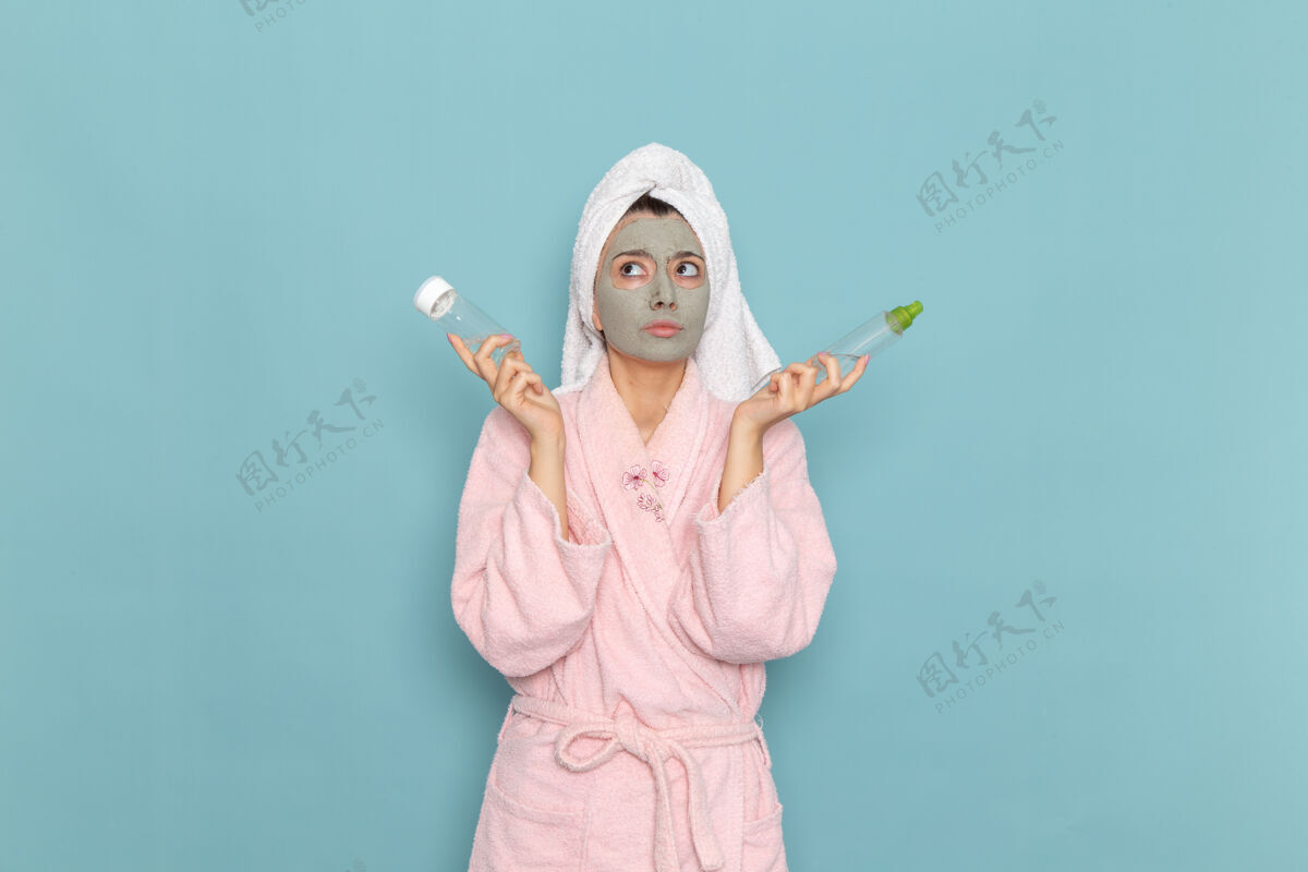 男人正面图年轻女性穿着粉色浴袍淋浴后拿着喷在蓝色墙上的美容水霜自护淋浴浴室景观人女人