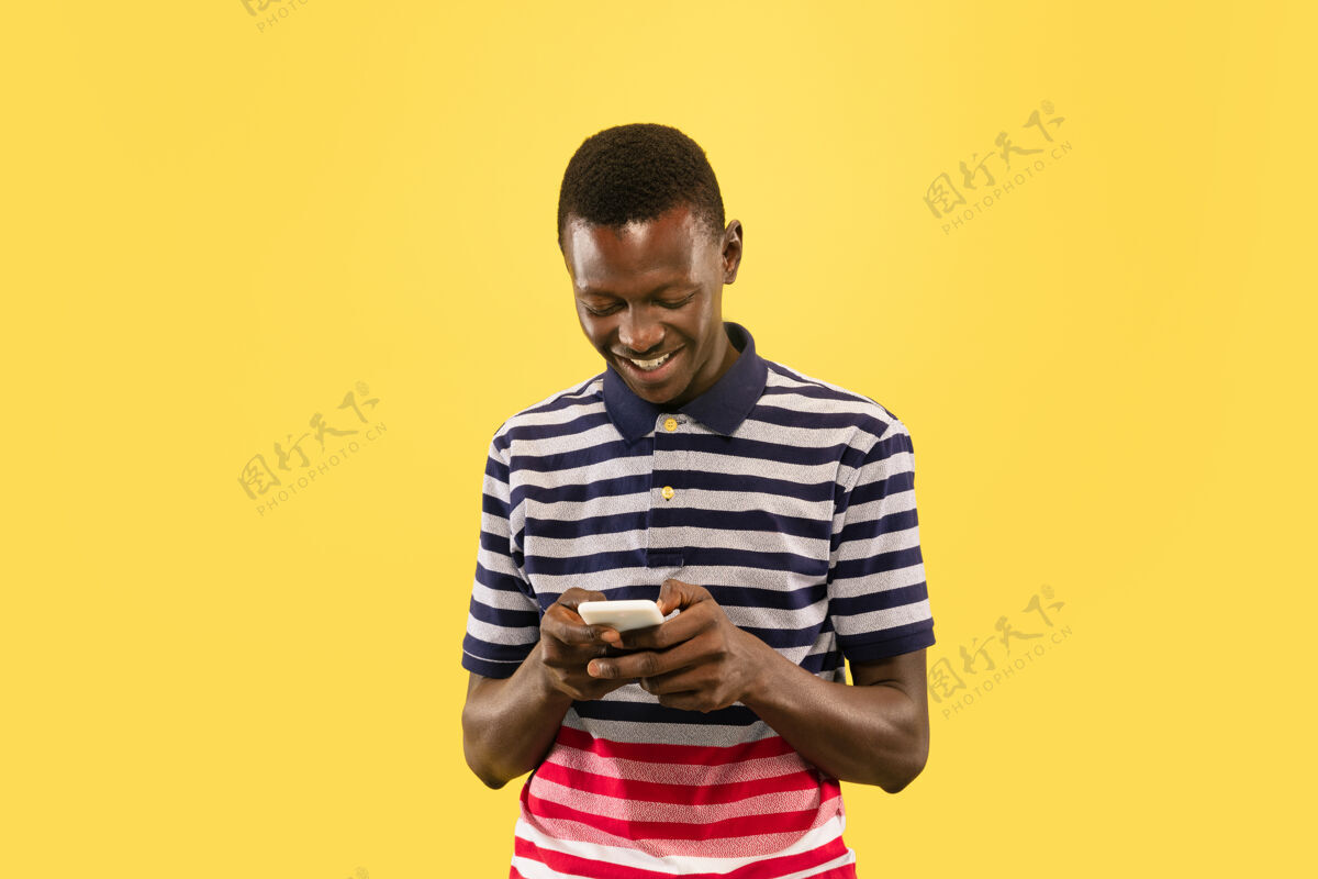 面部年轻的非洲裔美国男子用智能手机隔离在黄色的工作室背景下 面部表情美丽的男性半身肖像人类情感的概念 面部表情商人美国人帅帅