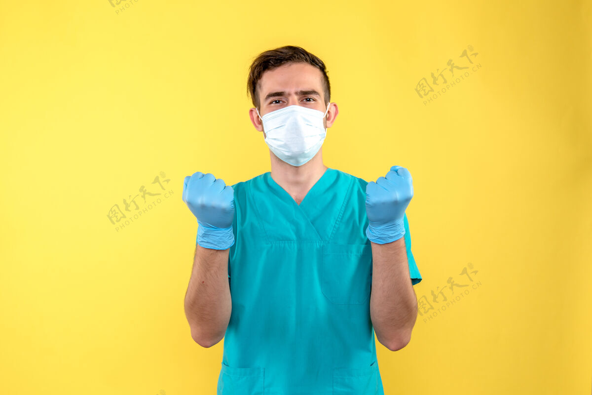人黄墙上戴着手套和口罩的男医生的正视图黄色手套人