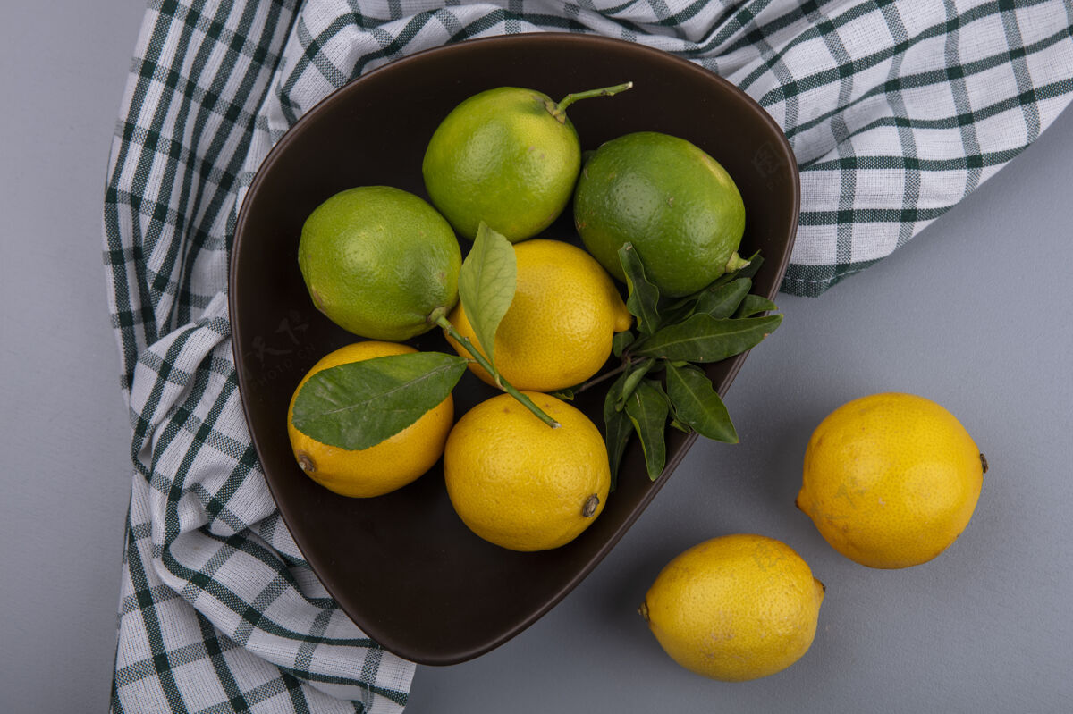顶部在灰色背景下 在格子毛巾上的碗里放着柠檬的酸橙柠檬水果柑橘