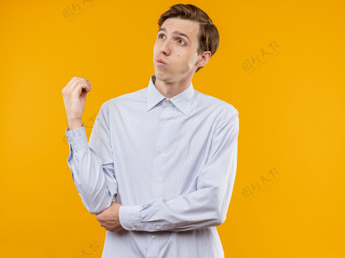 站身穿白衬衫的年轻人站在橘色的墙上 困惑地向一旁望去看橙色靠边