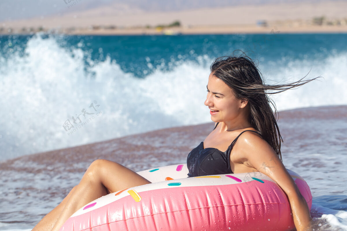 夏天一个快乐的女人 在海边有一个甜甜圈形状的游泳圈度假休闲娱乐的概念性感姿势特写