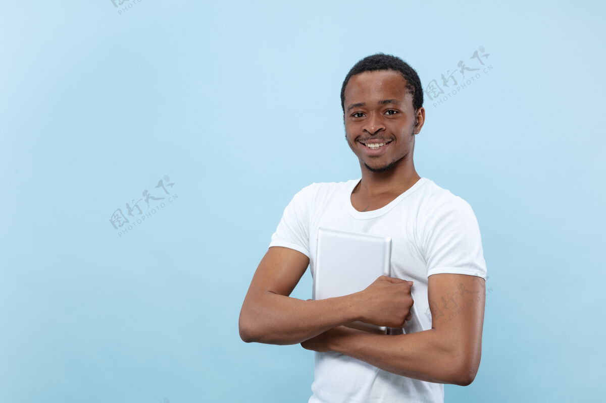 衬衫半身特写 蓝色背景 身穿白衬衫的非洲裔美国年轻男子人类情感 面部表情 广告 销售理念手持平板电脑 微笑看起来很开心行政人员男性事业